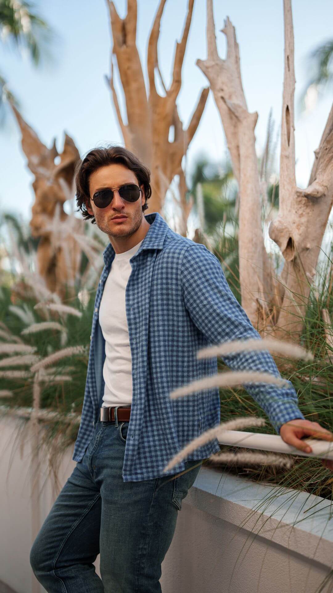 Model leaning on a ledge with open button up shirt and glasses